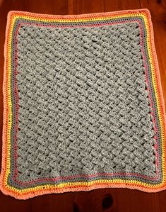 a crocheted dishcloth on a wooden floor with a wood table in the background