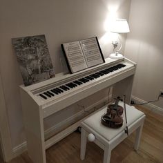 a white piano sitting on top of a hard wood floor next to a table lamp