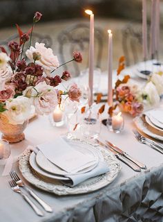 the table is set with white and pink flowers, silverware, candles and napkins