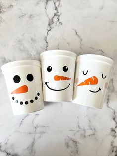 three cups with faces painted on them sitting next to each other, one has carrots in the shape of snowmen