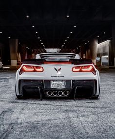 the rear end of a white sports car parked in a parking lot with lights on