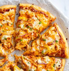 the pizza is cut into eight pieces and sits on top of wax paper with green onions