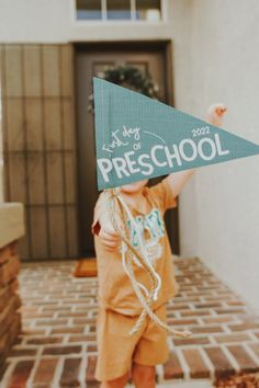 a young boy holding up a sign that says preschool in front of a house