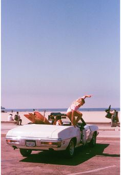 a woman standing on top of a white car with surfboards in the back seat