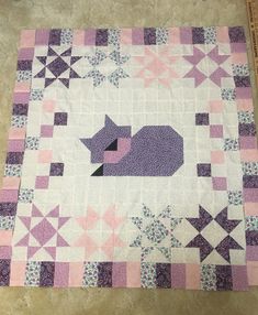 a pink and purple quilt with a cat on it's side, sitting on the floor