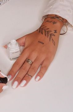 a woman's hand with tattoos on it next to a bottle of nail polish