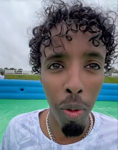 a close up of a person with curly hair and an inflatable pool behind him