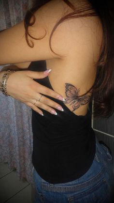 a woman with tattoos on her back is looking at the camera while wearing jeans and a black tank top