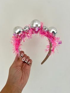 a hand is holding a pink headband with silver balls on it and some pink streamers