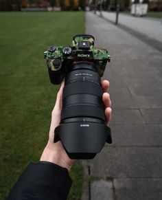 a person holding up a camera in front of some grass and trees on the sidewalk