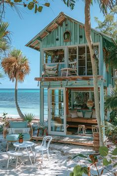 a house on the beach with chairs and tables in front of it, surrounded by palm trees