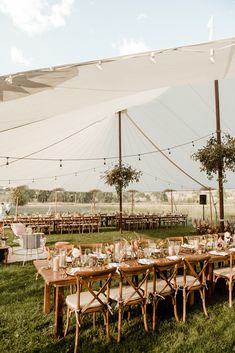 an outdoor tent with tables and chairs set up for a wedding reception in the grass