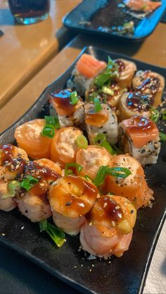 sushi is served on a black plate with chopsticks and garnishes