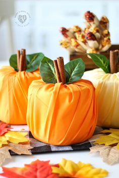 three small pumpkins with leaves and cinnamon stick sticking out of them on a table