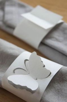 the folded napkins are decorated with white paper and a butterfly on one piece of fabric