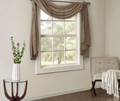 a chair and table in front of a window with drapes on the windowsill