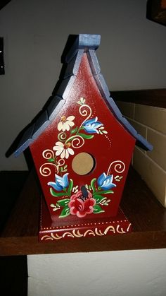 a red birdhouse with flowers painted on it's side sitting on a counter