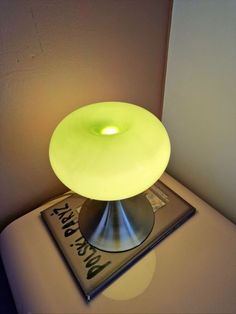 a yellow light sitting on top of a magazine next to a lamp that is turned on