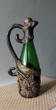 a green glass vase sitting on top of a woven table cloth next to a gray wall