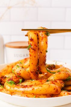 the food is being lifted by chopsticks into a bowl with sauce on it