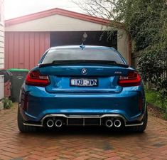 a blue bmw car parked in front of a red brick building with a white garage behind it