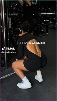 a woman squatting on the ground in front of a gym equipment rack with two people behind her