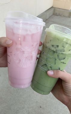 two starbucks drinks are being held up in front of the camera, one is green and the other is pink