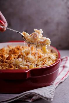 a red casserole dish with macaroni and cheese being scooped from it