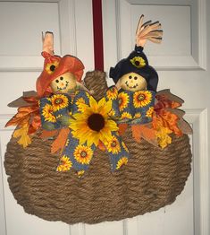 two scarecrows sitting on top of a basket with sunflowers and leaves