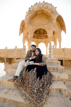 two people sitting on steps in front of a gazebo with an intricately designed dress