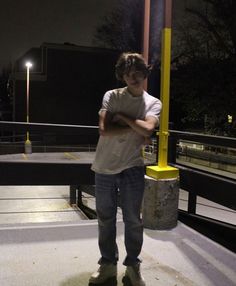 a young man standing next to a yellow light pole at night with his arms crossed