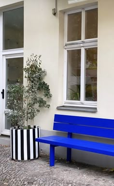 a blue bench sitting in front of a white building next to a potted plant