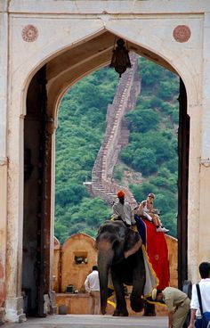 two men riding on the back of an elephant in front of a stone building with stairs