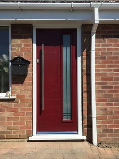 a red front door on a brick house with white trim and sidelights, next to a black mailbox