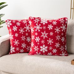 two red and white snowflake pillows sitting on a couch next to a potted plant