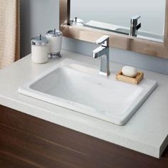 a bathroom sink sitting under a mirror next to a counter top with soap dispenser