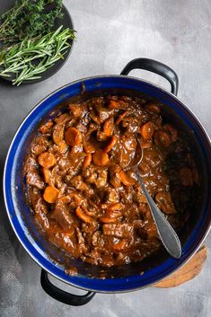 a blue pot filled with meat and carrots on top of a table next to green beans