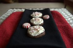 three cookies with white frosting and candy canes sit on a black plate next to a red towel