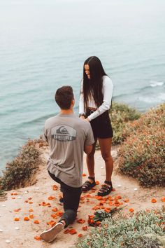 a man and woman walking up a hill next to the ocean covered in orange flowers