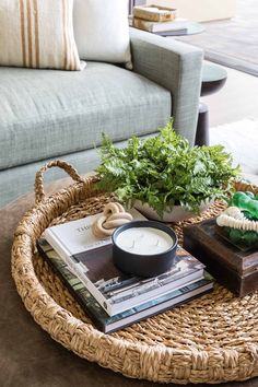 a wicker coffee table with books, candle and plant on it in front of a couch