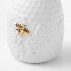 a white ceramic vase with a gold bee on it's side, sitting against a white background