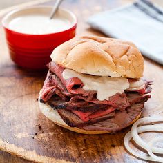 a roast beef sandwich on a wooden cutting board next to a bowl of ranch dressing