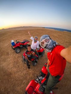 three people on four wheelers in the middle of an open field with one person waving