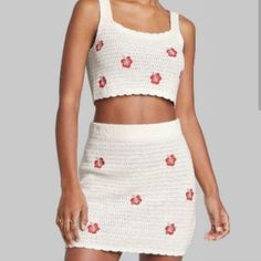 a woman wearing a white knitted skirt and crop top with red flowers on it