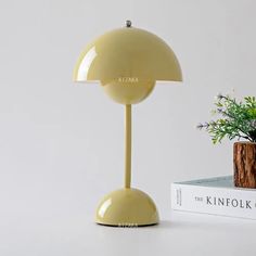 a yellow lamp sitting on top of a table next to a book and potted plant