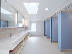 an empty bathroom with blue stalls and skylights above the sinks in front of them