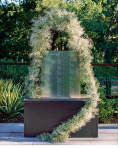 a sculpture with white flowers on it in the middle of a sidewalk near some bushes