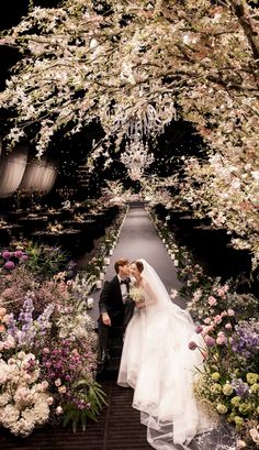 a bride and groom are kissing in front of an archway with flowers all around them