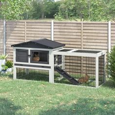 an outdoor rabbit hut with stairs to the top and door open, in front of a fence