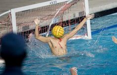 a man jumping up to hit a volley ball in the water while people watch from the sidelines